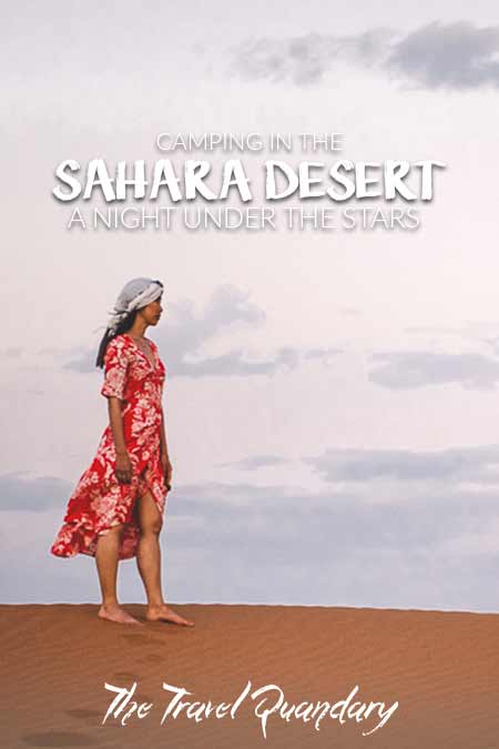 A woman in a red dress stands on a sand dune under the early moon at dusk, Sahara Desert Morocco