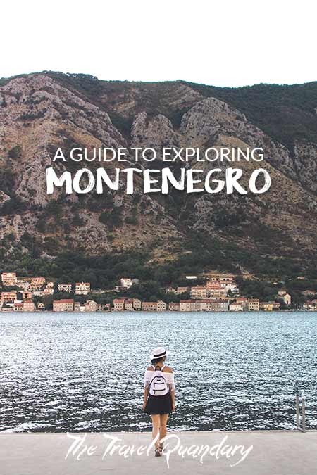 A woman with a white hat and white backpack stands on the edge of the water overlooking the Bay of Kotor, Montenegro