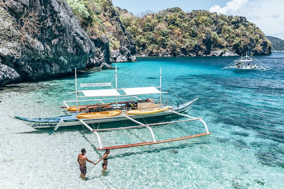 A couple hold hands next to their tour boat in the water on Paradise Beach, El Nido