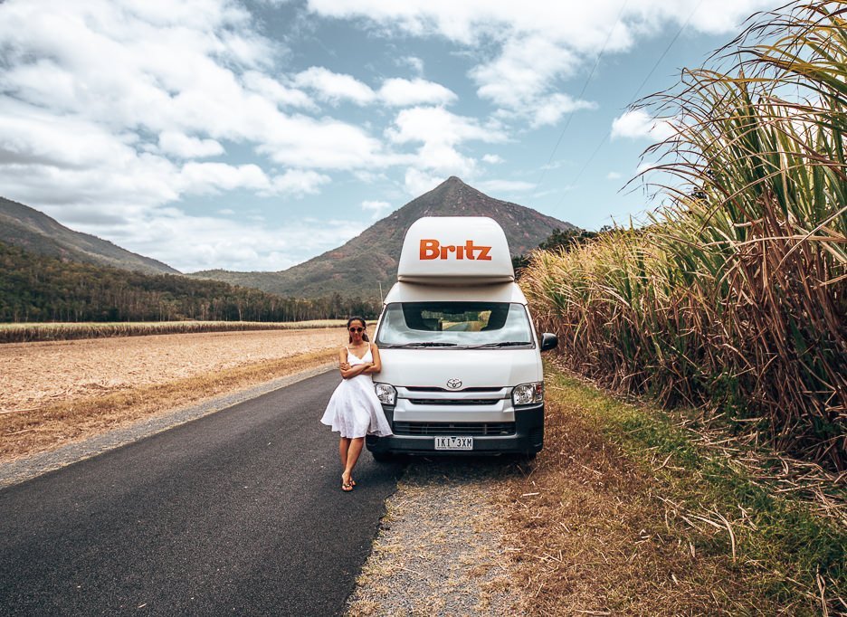A girl in a white dress stands next to a Britz campervan in Tropical North Queensland