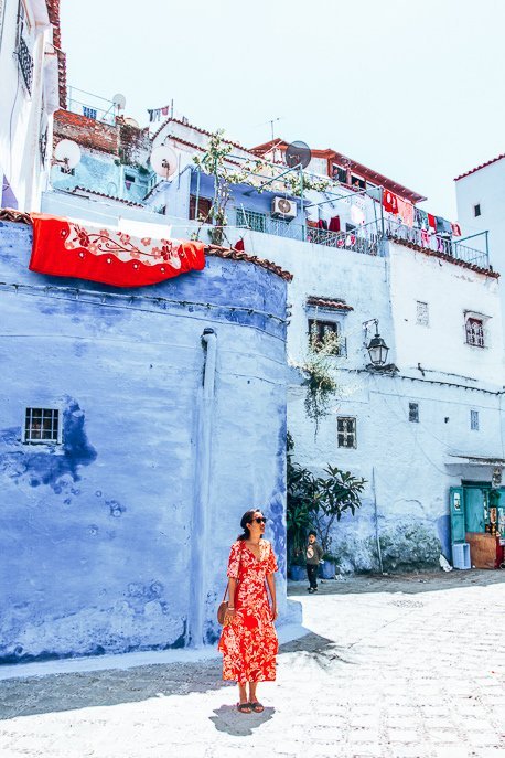 A woman dressed in a red dress stands in an empty square in Chefchaouen, Morocco