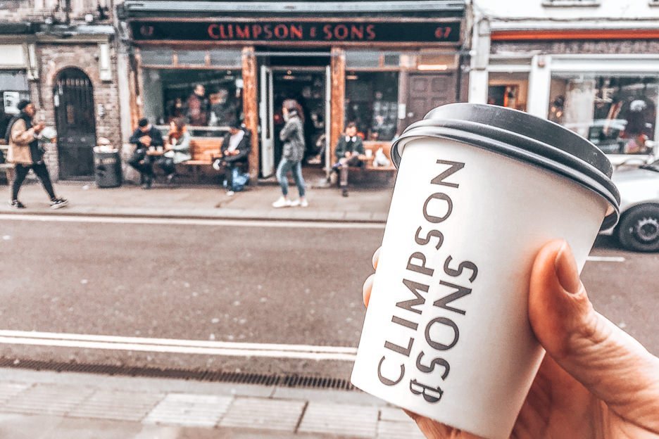 Holding a takeaway cup from Climpson & Sons in front of the Climpson & Sons cafe in East London