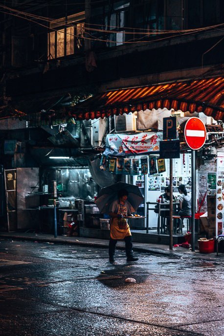 A woman carries a tray of food in the drizzly rain at night in Mong Kok, Hong Kong