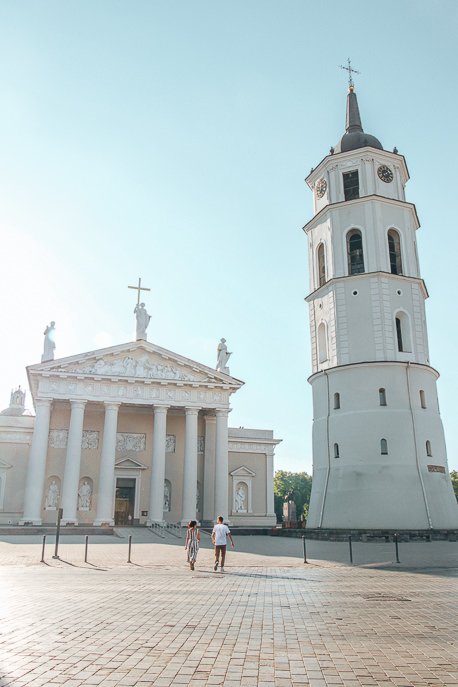 A couple walk in front of Vilnius Cathedral at sunrise, Vilnius - 5 Things When Dating Travelling