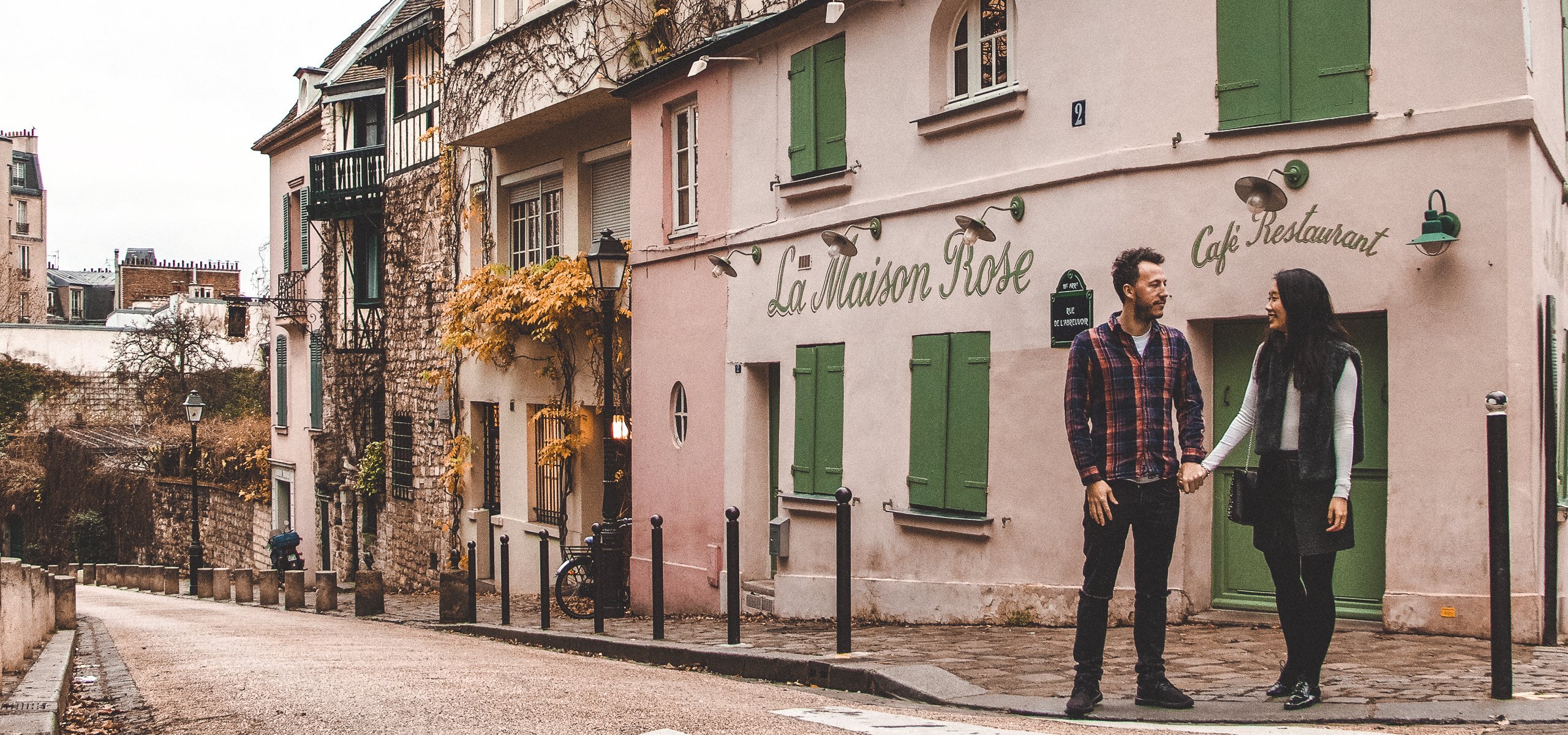 A couple holds hands In front of La Maison Rose, Montmartre, Paris - Travelling with Parents